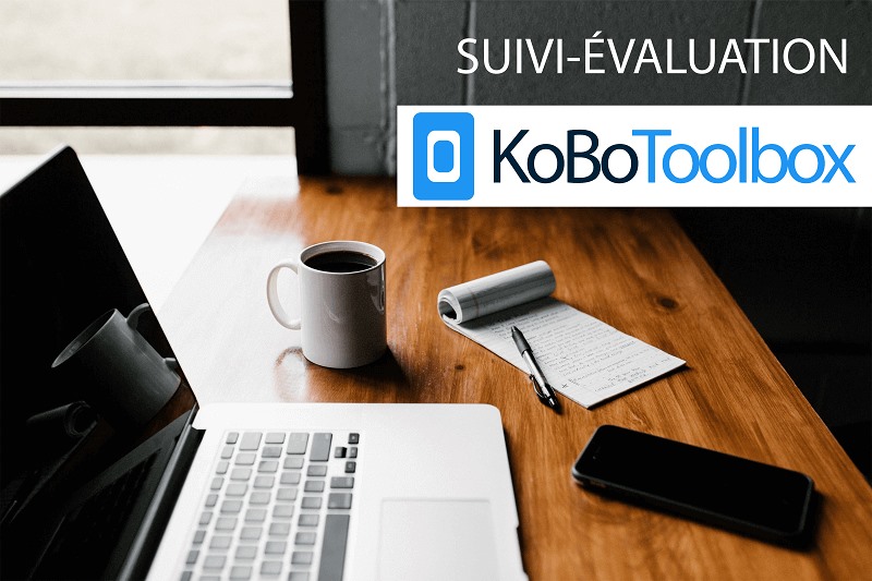 Picture of a desk with a laptop, coffee mug, smartphone, notepad and KoBoToolbox logo at top right